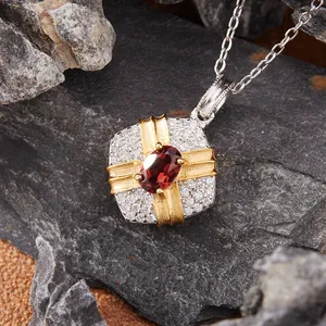 Detailed macro view of a gift-box shaped silver pendant with a red garnet center