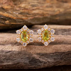 Macro view of gold flower earrings with green center gemstone and diamond accents