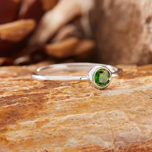 Primo piano di un anello in argento con gemma verde tonda incastonata su uno sfondo di roccia.