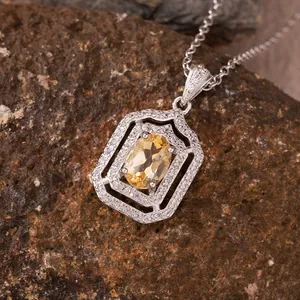 Detailed view of a yellow citrine pendant with silver frame on a natural stone surface.