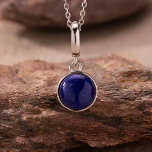 Macro view of round lapis lazuli pendant on silver chain against natural stone