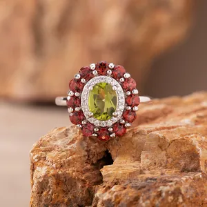 Detailaufnahme eines silbernen Blumenrings mit grünem Peridot und roten Granaten