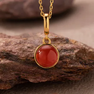 Close-up of a natural red agate pendant with gold-plated sterling silver chain on rock.