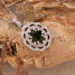 Detailed macro view of a dark green gemstone pendant with floral silver halo on natural rock.