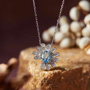 Detailed close-up of a silver daisy pendant necklace with a brilliant blue oval gemstone.