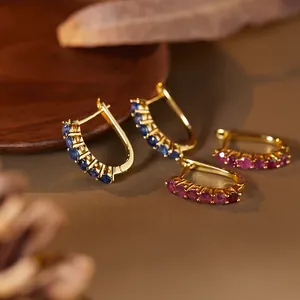 Macro detail of S925 gold-plated earrings with pavé-set natural sapphire and ruby gems.