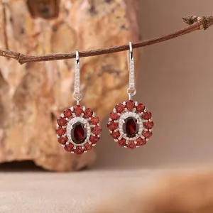 Detailaufnahme von silbernen Ohrringen mit roten Edelsteinen an einem Ast hängend