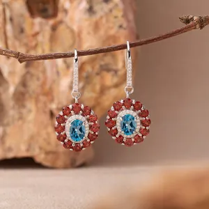 Detailansicht von Silberohrringen mit blauem Topas und rotem Granat in Blumenform.