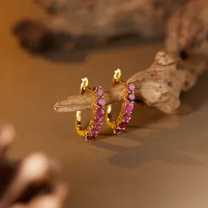 Macro detail of gold hoop earrings with pink ruby gemstones on a natural branch
