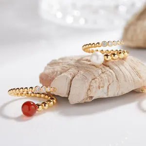 Primer plano detallado de anillos de plata dorada con ágata roja y perla sobre piedra