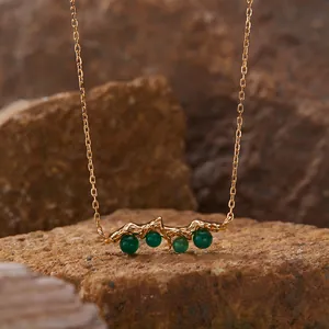 Close-up of a textured gold-tone necklace pendant featuring round green agate stones.