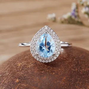 Primo piano di anello con gemma blu a goccia e doppio halo in argento S925 lucido.