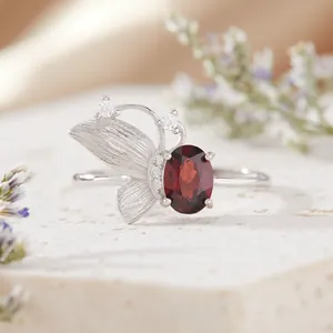 Primer plano de un anillo de mariposa de plata con un elegante granate rojo ovalado