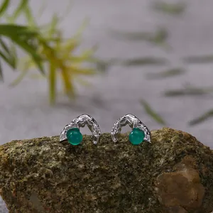 Macro detail of silver stud earrings with vibrant green agate stones on a rock prop.