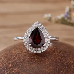 Primo piano di un anello con gemma rosso scuro a forma di pera e un doppio alone di pietre chiare