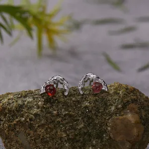 Close-up of S925 silver stud earrings with red garnet stones on a textured rock