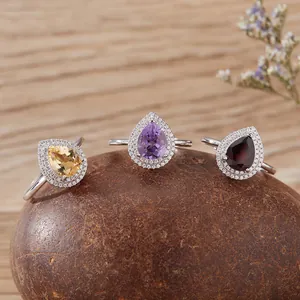 Dettaglio di tre anelli in argento con pietre naturali a forma di goccia su una pietra.