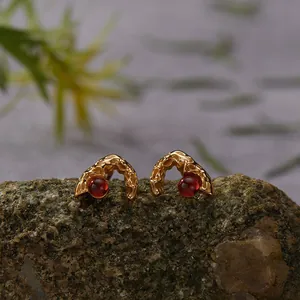 Close-up of gold lava texture stud earrings set with red garnet gemstones on a rock