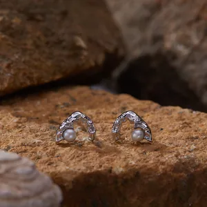 Close-up of silver mountain-shaped earrings with pearls on a natural rock surface.