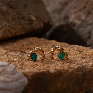 Macro view of textured gold stud earrings with green agate set on natural rocks background