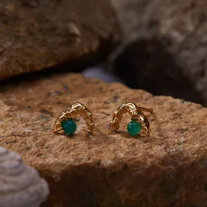 Detailed view of irregular gold earrings featuring green agate stones on rock