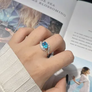 Close-up of an elegant S925 sterling silver ring with a blue gemstone on a model's hand.