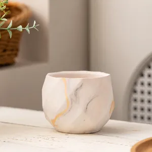 Detailopname van een minimalistische keramische vetplantenpot met goudmarmeren patroon.