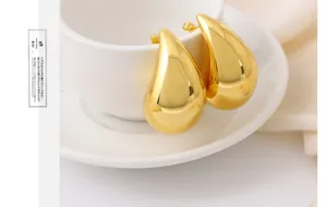 Primer plano de pendientes de gota de metal liso dorado en una taza blanca
