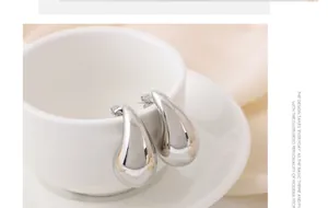Vista detallada de pendientes de gota de metal plateado minimalistas colgados en una taza