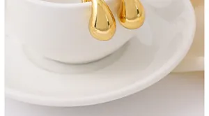 Primer plano detallado de pendientes de gota de agua dorados brillantes en una taza blanca
