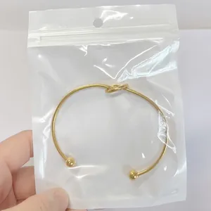 Detailed view of gold stainless steel knot cuff bracelet in clear zip-top packaging