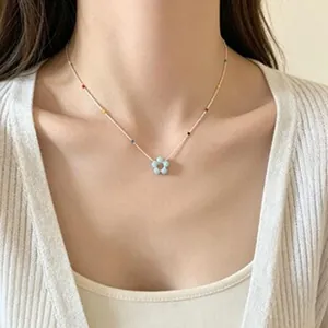 Model wearing a delicate gold necklace with a blue flower pendant and colorful beads