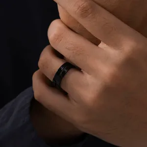 Close-up view of a minimalist black stainless steel ring worn on a male hand in dark lighting.