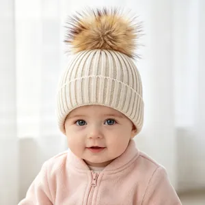 Detail view of a baby wearing a cream ribbed knit hat with a large faux fur pom-pom