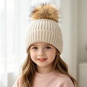 Close-up of a child wearing a cream ribbed knit beanie with a fluffy faux fur pom pom