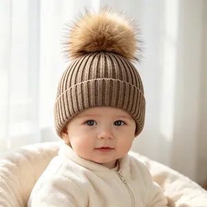 Close-up of a baby wearing a brown ribbed knit beanie with a faux fur pom-pom