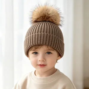 A professional close-up of a child wearing a brown ribbed knit beanie with a fur pom-pom