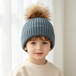 Adorable child wearing a blue ribbed knit beanie with a large brown faux fur pom-pom