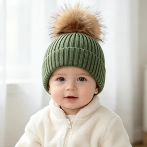 Close-up of baby wearing green ribbed knit beanie with soft brown faux fur pom pom
