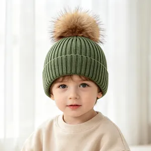 Close-up of a green knit children's beanie with a soft brown faux fur pom-pom