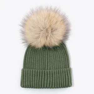 Detail view of a green ribbed knit beanie with a large fluffy faux fur pom-pom