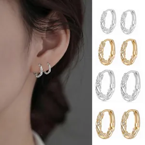 Detail view of wavy zircon-encrusted hoop earrings in silver and gold finishes