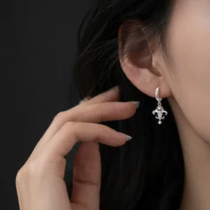 Close-up detail of an elegant silver hoop earring with a cross dangle on a model's ear
