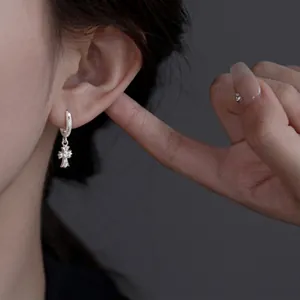 Detailed shot of a silver cross hoop earring with sparkling rhinestones on an ear