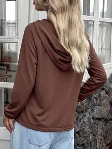 Vista trasera detallada de una cómoda sudadera con capucha marrón para mujer en una pared
