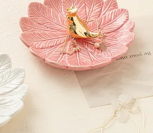 Gros plan d'un plateau à bijoux en céramique rose en forme de feuille avec oiseau doré