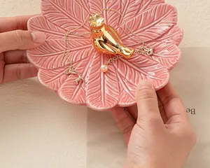 Détail d'un plateau à bijoux en céramique rose en forme de feuille avec un oiseau.