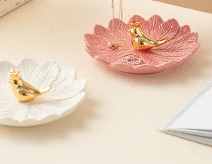 Gros plan de plateaux à bijoux en céramique en forme de feuille avec oiseau doré