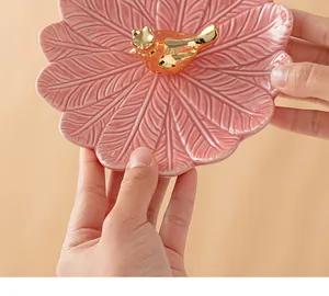 Détail du plateau en céramique rose en forme de feuille avec oiseau doré élégant