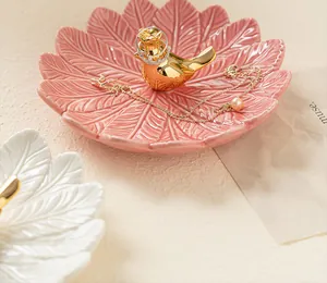 Gros plan d'un plateau à bijoux en céramique rose en forme de feuille avec un petit oiseau doré.
